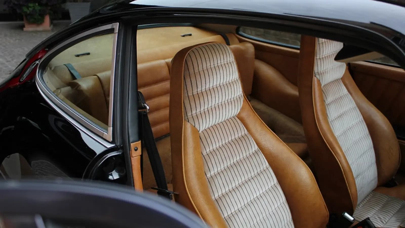 Clean tan leather and striped fabric seats inside a classic black car with the door open