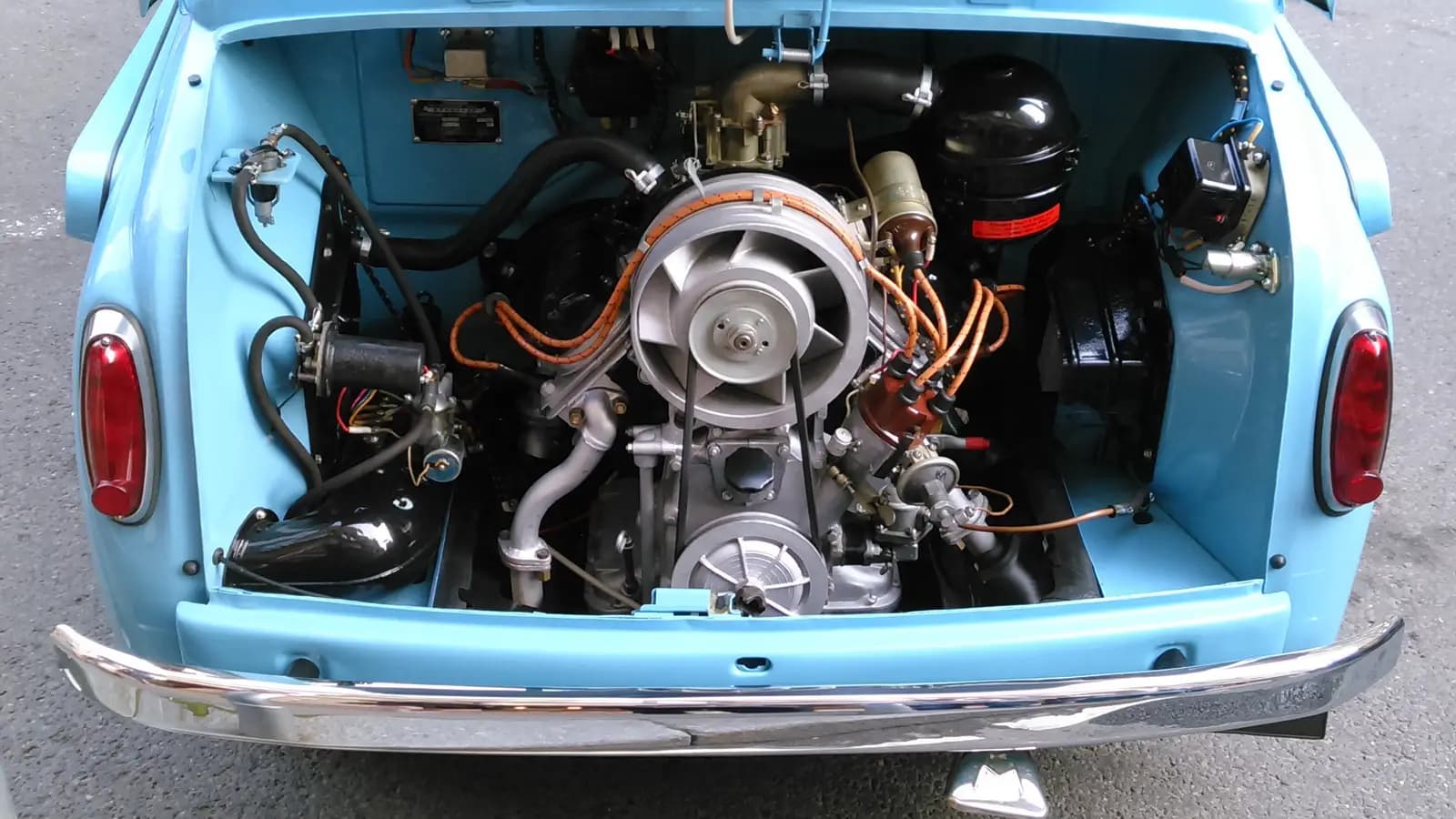 Open rear engine bay of a light blue vintage car showing the clean engine, fan, wiring, and mechanical parts
