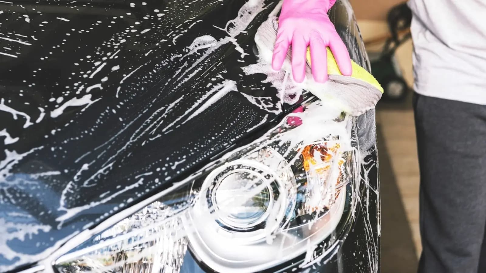 Person wearing a pink glove washing a black car with a sponge and white soap suds