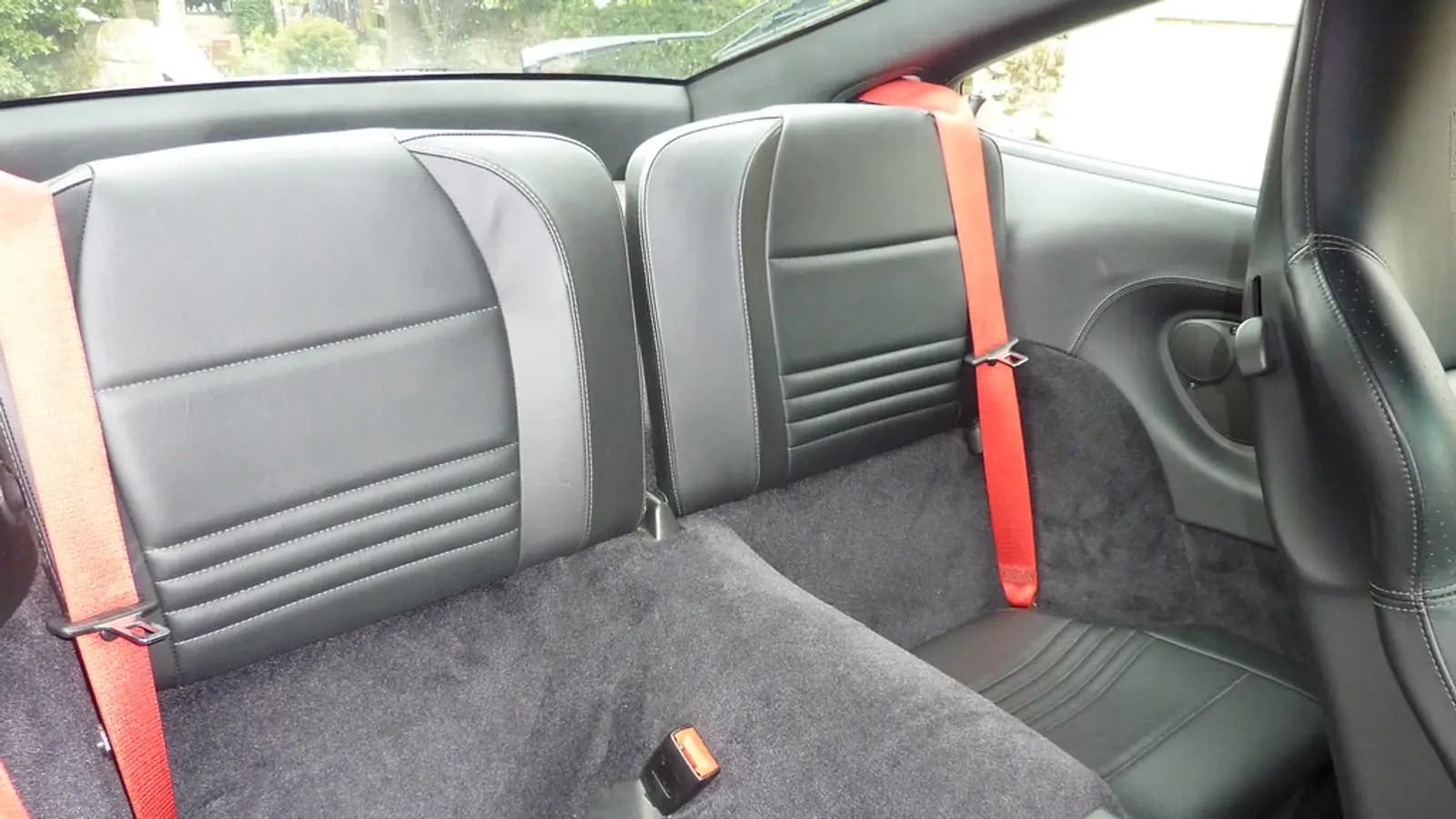 Rear interior of a car with black leather seats, red seatbelts, and dark grey carpet