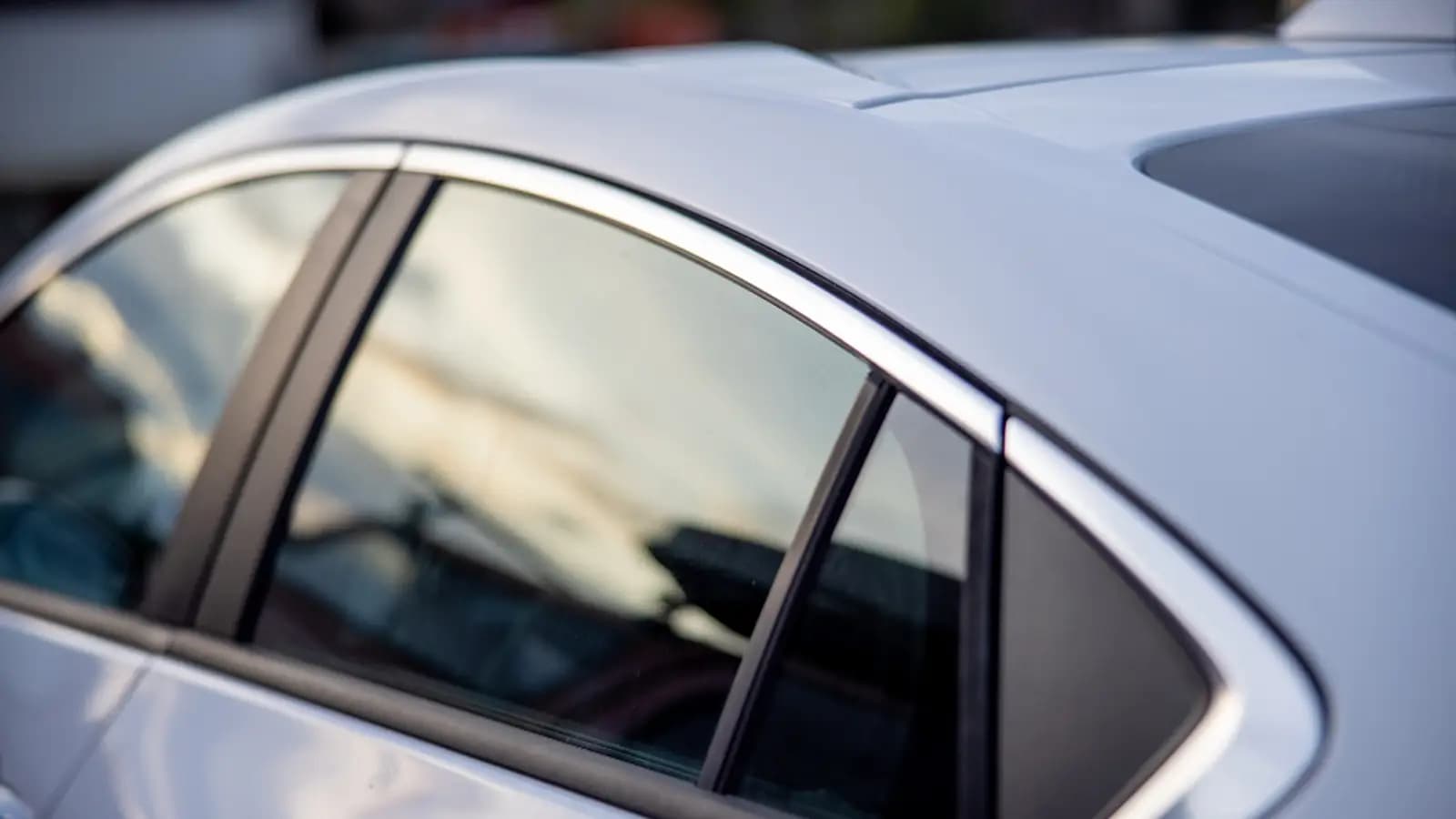Close up of a clean white car's side windows and roofline, with reflections of the sky on the glass and paint