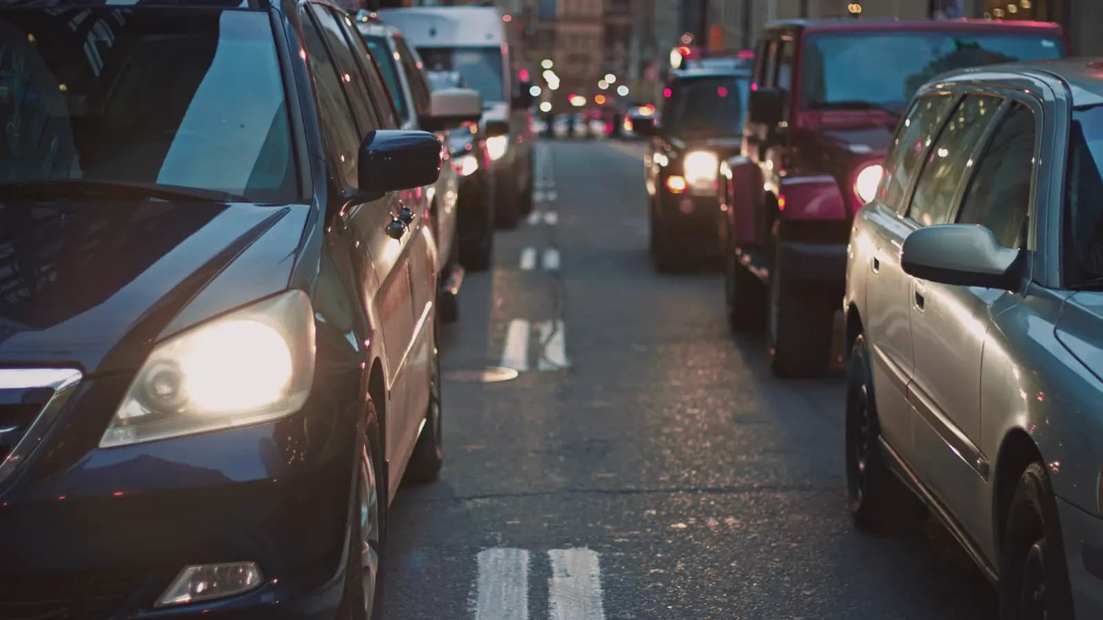 Cars in evening traffic with headlights on, the front left car's headlight shows a slight yellow tint