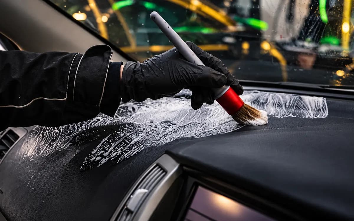 Gloved hand brushing cleaning foam across a car dashboard
